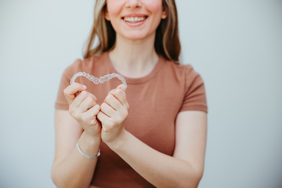 woman holding invisalign clear aligners in a heart shape to show the benefits of invisalign